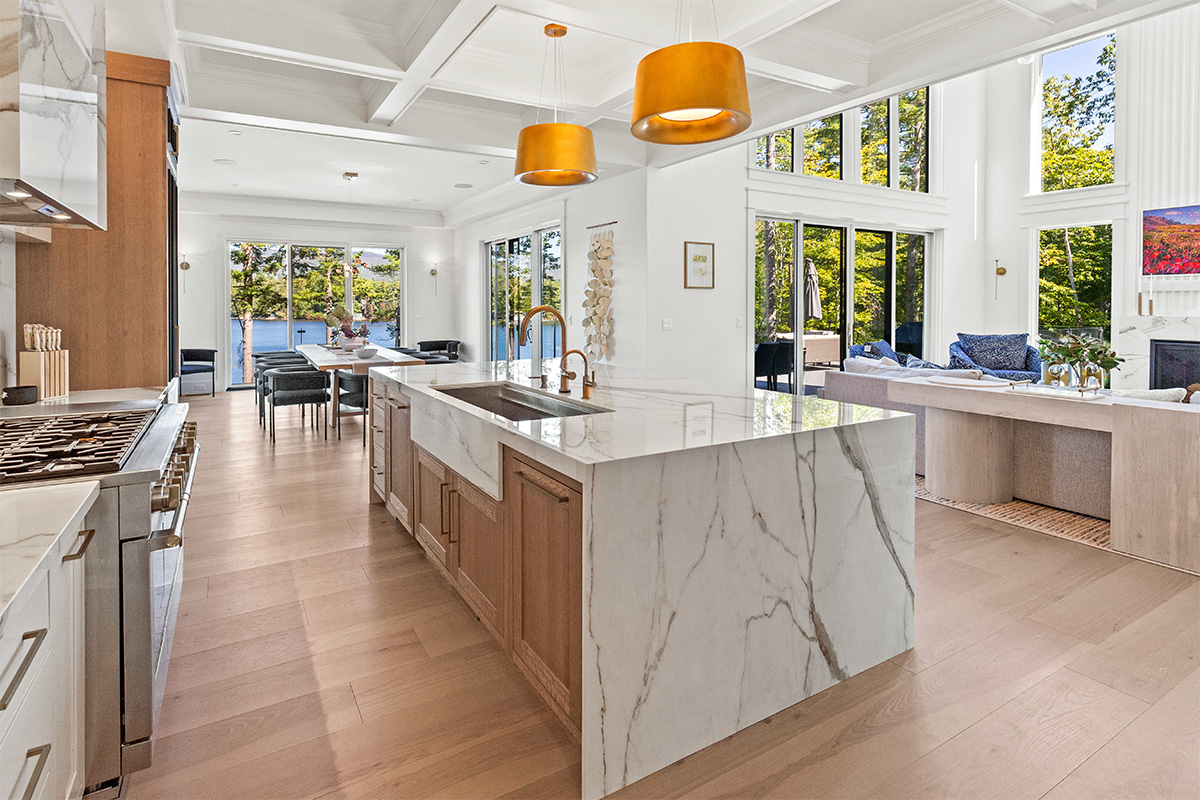 White kitchen cabinets with brown stained island with marble waterfall counter and hood
