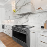 White kitchen cabinets with brown stained island with marble waterfall counter and hood