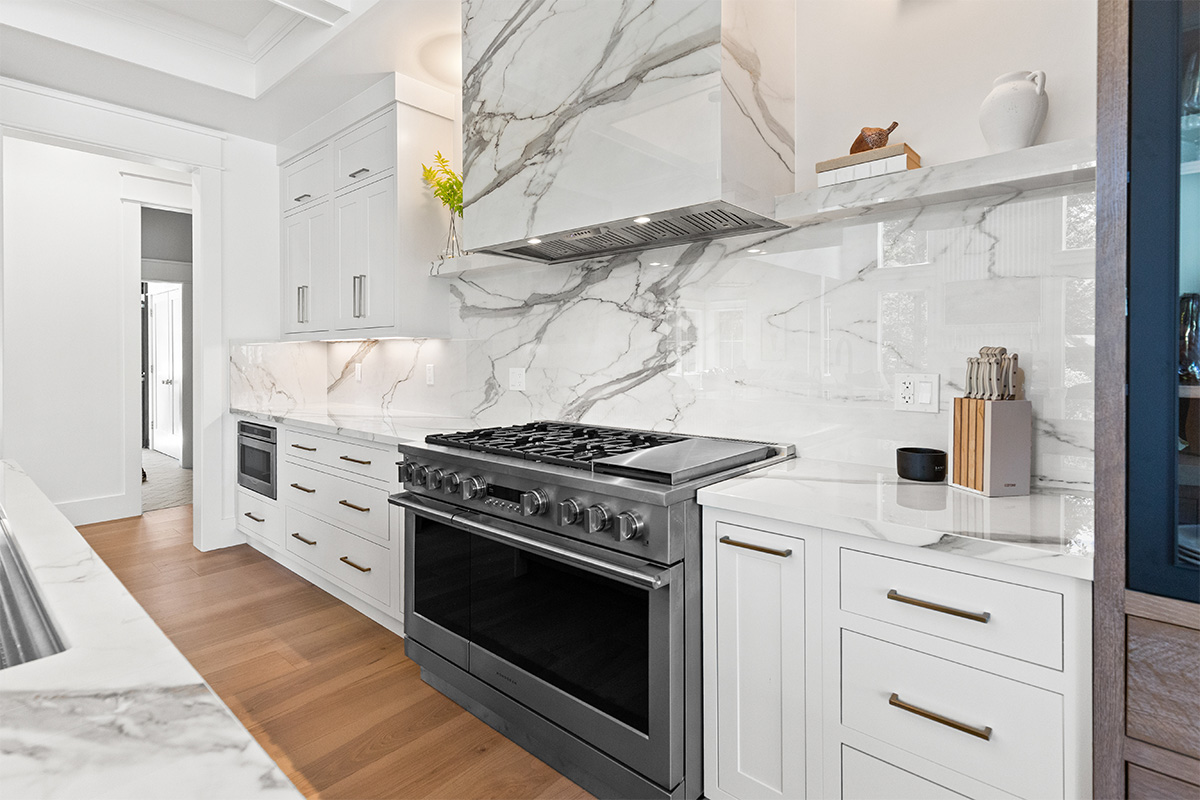 White kitchen cabinets with brown stained island with marble waterfall counter and hood