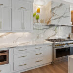 White kitchen cabinets with brown stained island with marble waterfall counter and hood