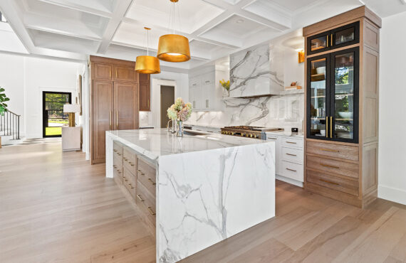 White kitchen cabinets with brown stained island with marble waterfall counter and hood