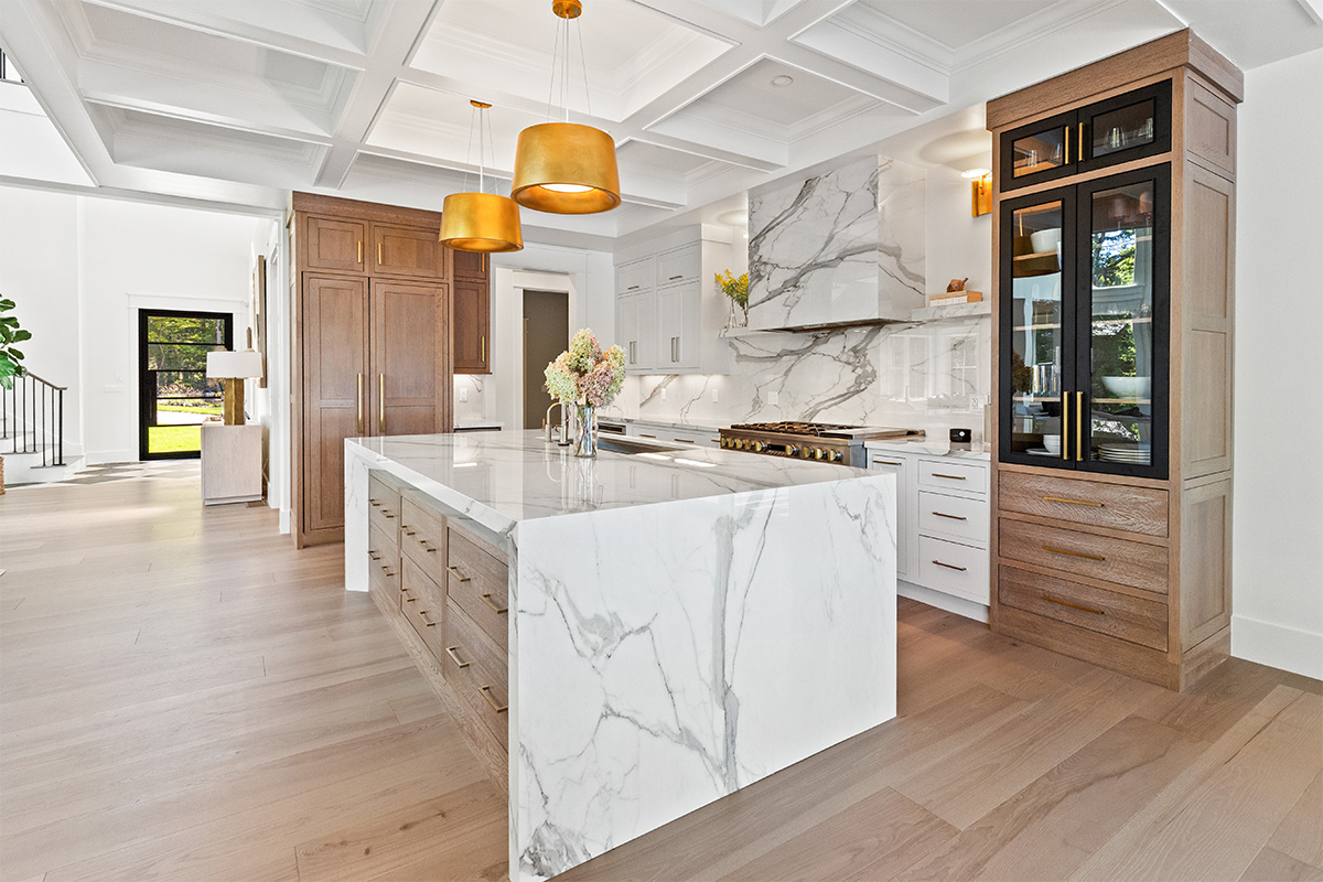 White kitchen cabinets with brown stained island with marble waterfall counter and hood