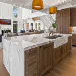 White kitchen cabinets with brown stained island with marble waterfall counter and hood