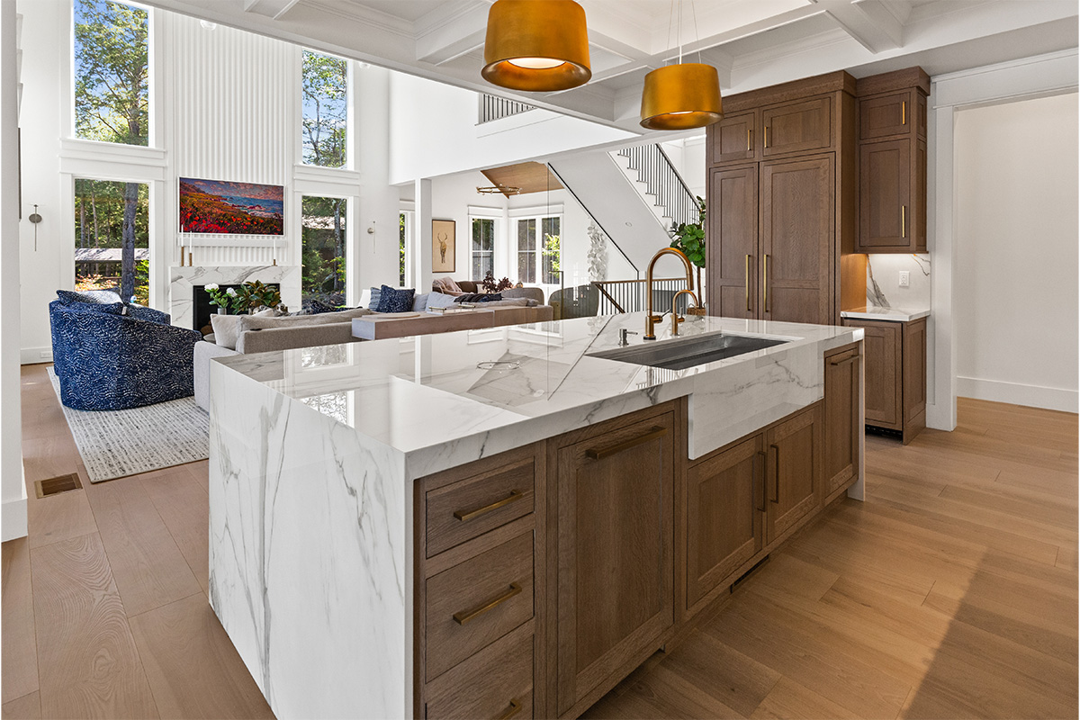 White kitchen cabinets with brown stained island with marble waterfall counter and hood
