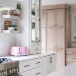 White kitchen and island with light brown stained cabinets in the distance