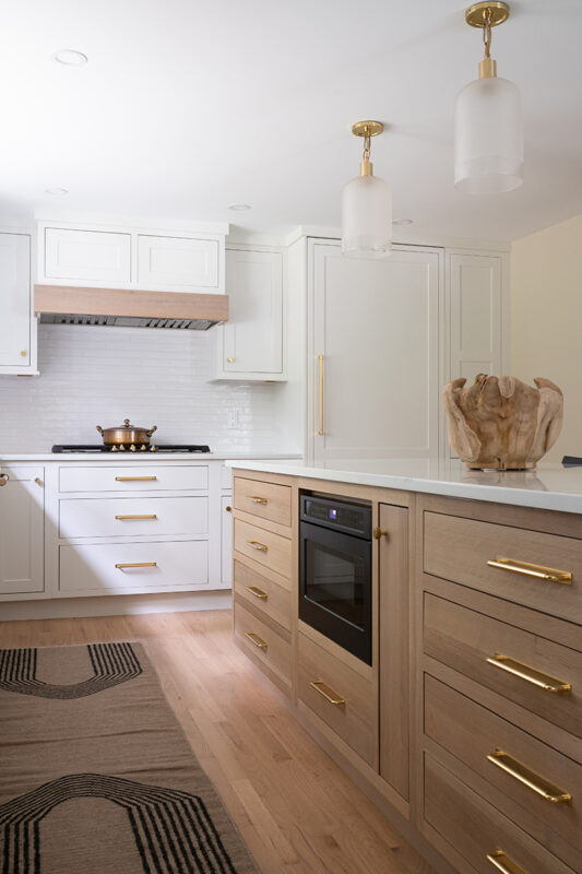 Kitchen with White perimeter cabinets and Quartersawn White Oak island cabinets stained in light brown Pampas finish.