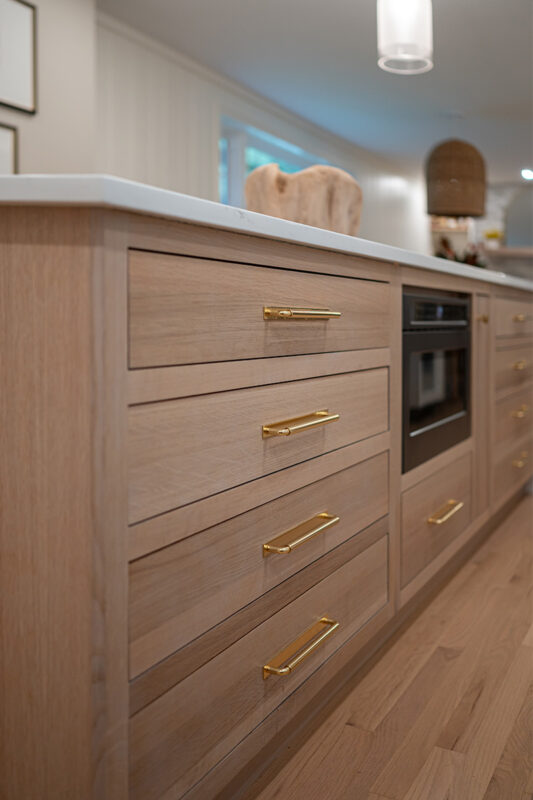 Kitchen with White perimeter cabinets and Quartersawn White Oak island cabinets stained in light brown Pampas finish.