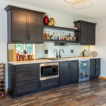 Dark stained bar cabinets with floating shelves, sink, microwave, and wine fridge.