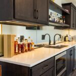 Dark stained bar cabinets with floating shelves, sink, microwave, and wine fridge.