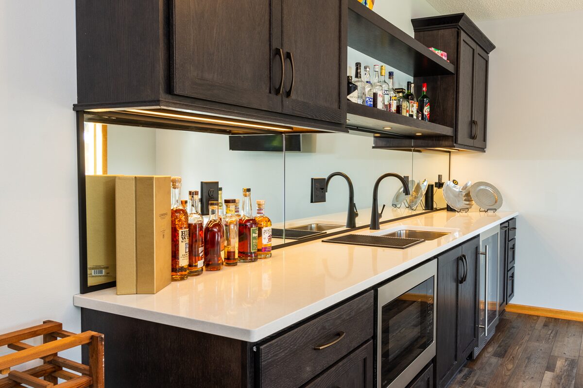 Dark stained bar cabinets with floating shelves, sink, microwave, and wine fridge.