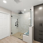 Gray bathroom linen cabinet next to a shower with glass walls