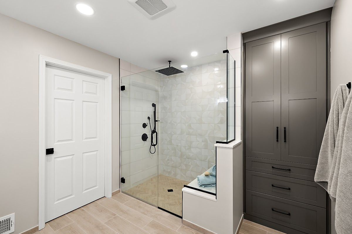 Gray bathroom linen cabinet next to a shower with glass walls