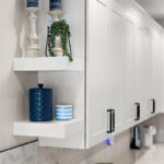 White floating shelves attached to the side of white kitchen cabinets