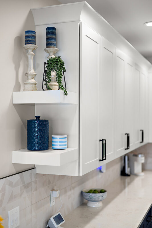 White floating shelves attached to the side of white kitchen cabinets