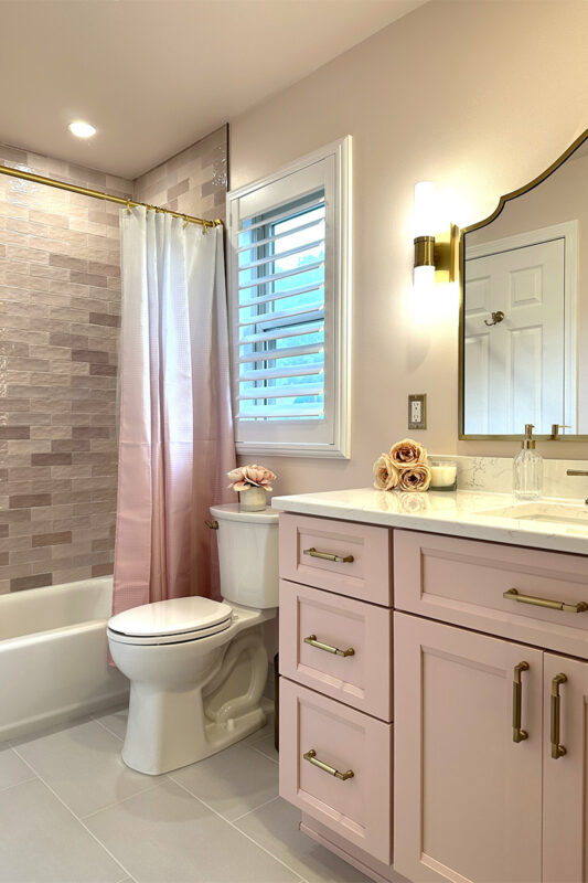 Pink bathroom with pink tile and single-sink vanity and gold rimmed mirror