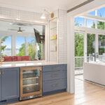 Blue painted bar cabinets with large living room with full height windows.