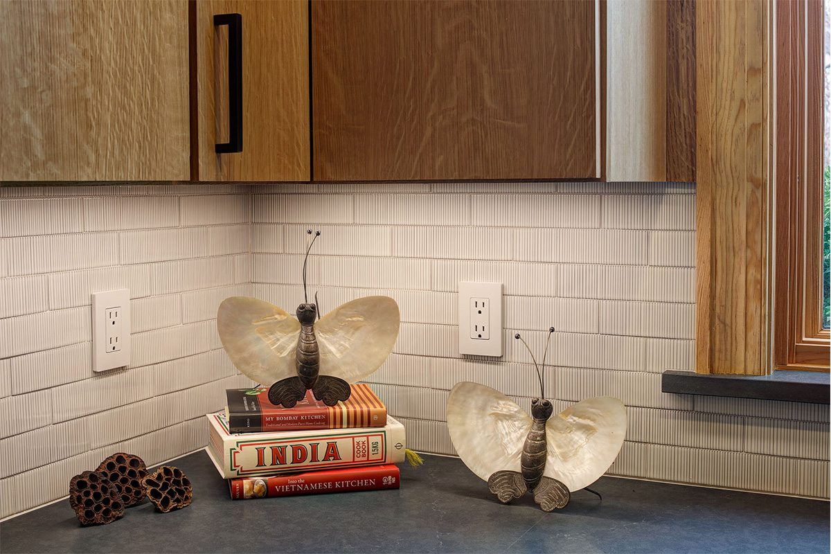 Light brown kitchen cabinet with close up of tile backsplash and items on a counter.