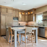 Cashew-stained kitchen perimeter cabinets and gray-painted island with legs and stools.