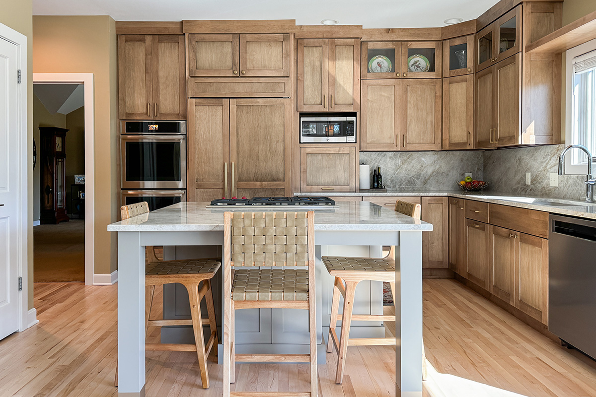 Cashew-stained kitchen perimeter cabinets and gray-painted island with legs and stools.
