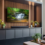 Contemporary entertainment center with gray painted cabinets and stained slatted back wall behind a large mounted tv.