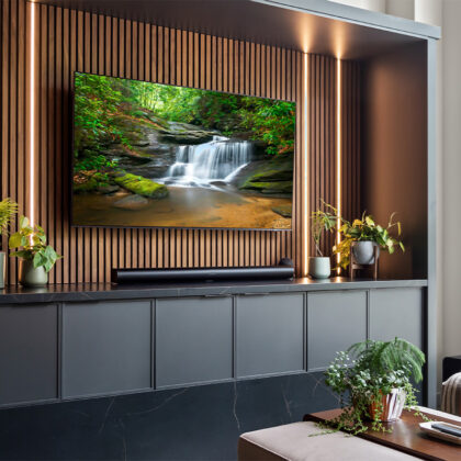Contemporary entertainment center with gray painted cabinets and stained slatted back wall behind a large mounted tv.
