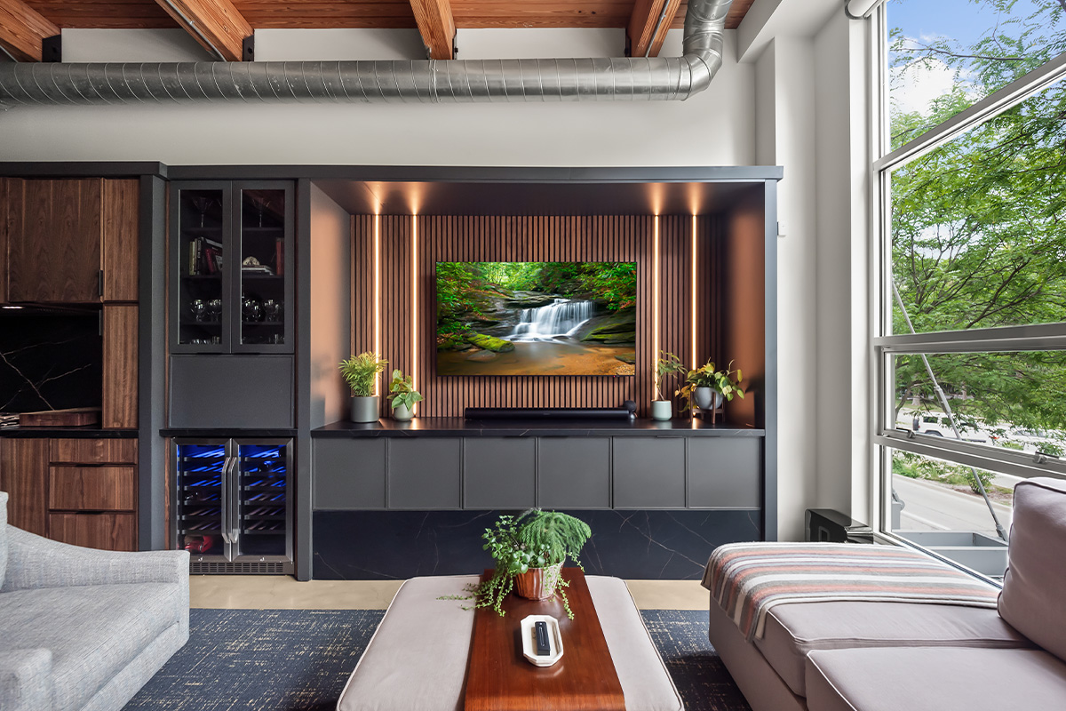 Contemporary entertainment center with gray painted cabinets and stained slatted back wall behind a large mounted tv.