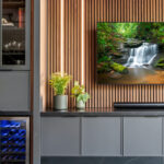 Contemporary entertainment center with gray painted cabinets and stained slatted back wall behind a large mounted tv.