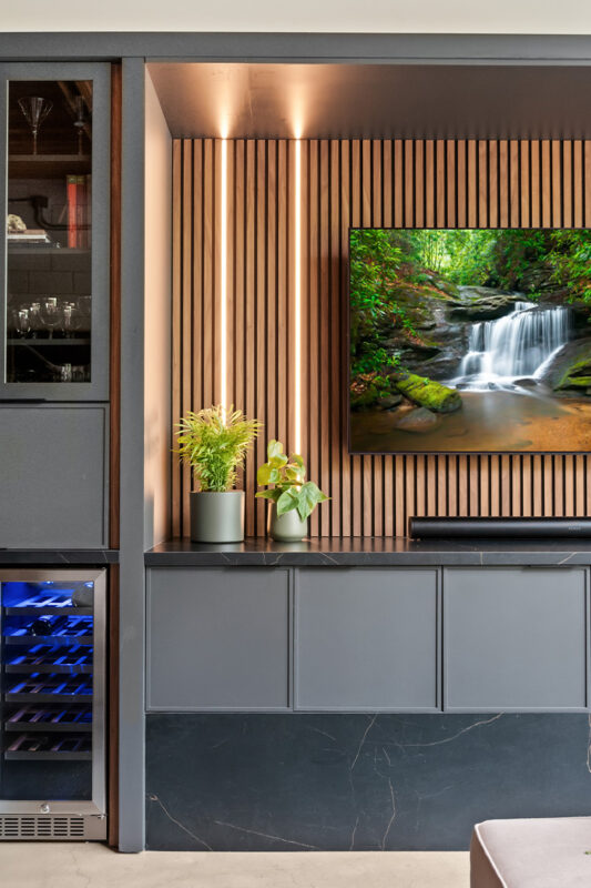 Contemporary entertainment center with gray painted cabinets and stained slatted back wall behind a large mounted tv.
