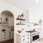 White kitchen cabinets with large hood. View looks into a pantry in arched walkway.
