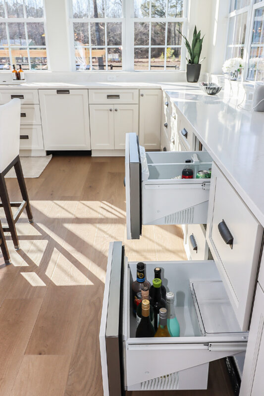 White kitchen cabinets with wine cooler drawers pulled out.