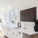 White kitchen cabinets with large row of windows above.