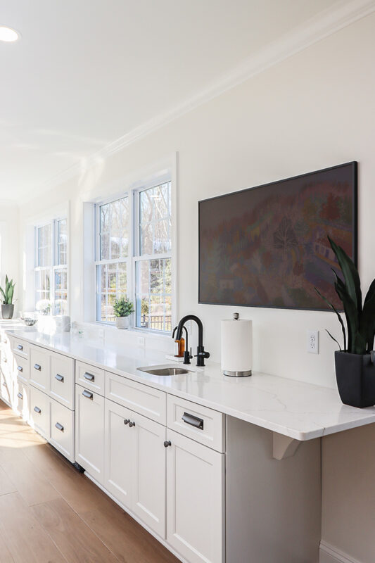 White kitchen cabinets with large row of windows above.