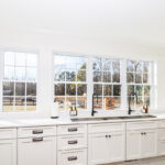 White kitchen cabinets with large row of windows above.