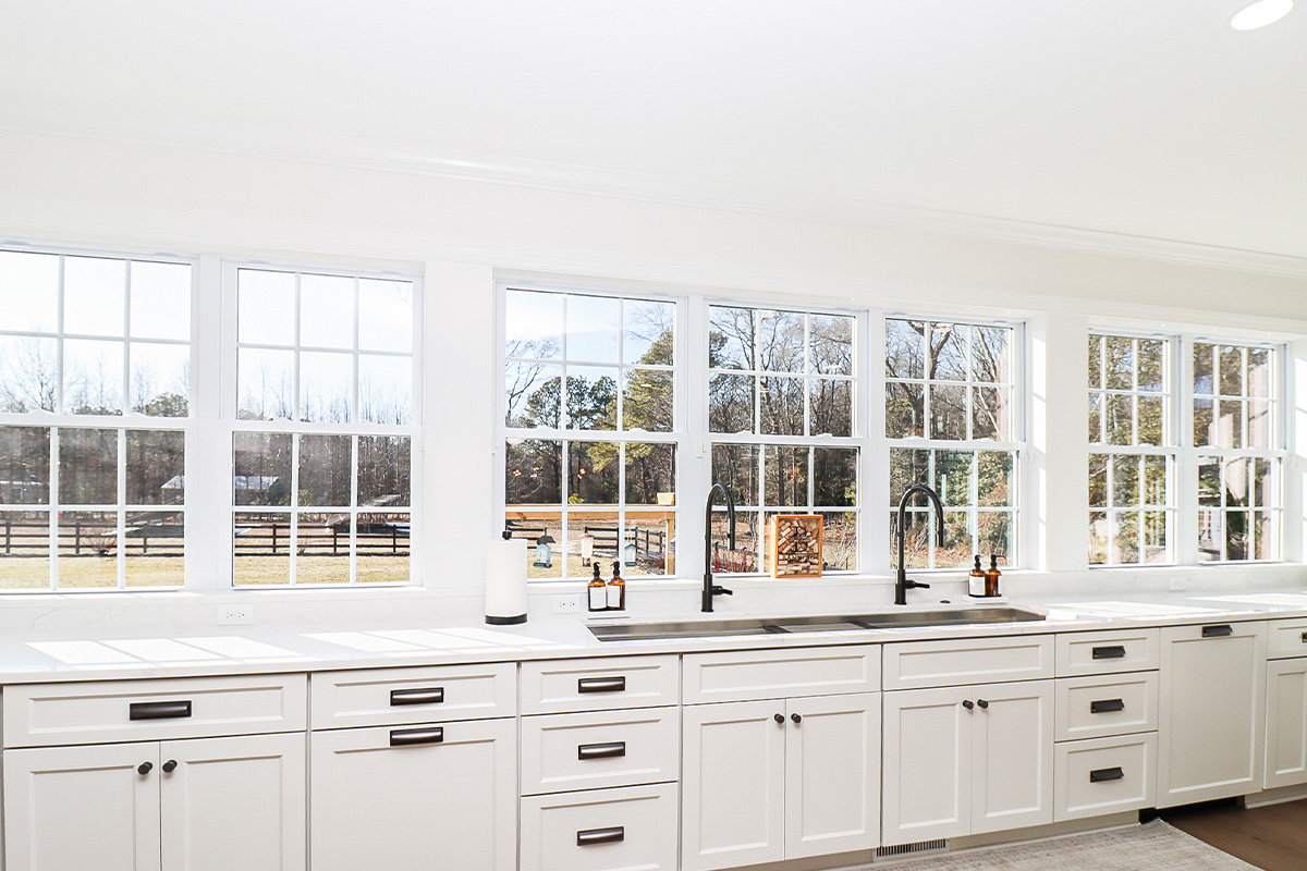 White kitchen cabinets with large row of windows above.