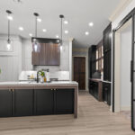 Light gray and black painted kitchen cabinets with walnut accent hutch cabinets, with a pullout walnut table connected to the island.
