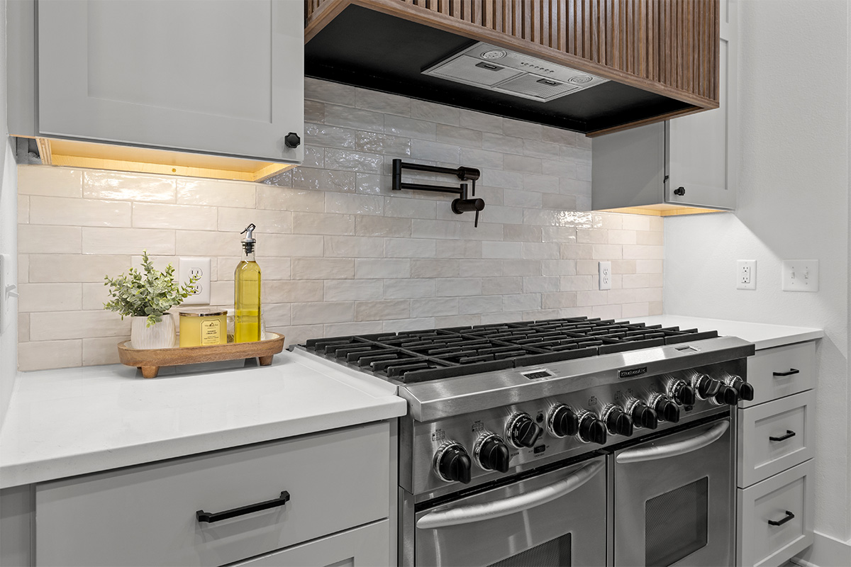 Gray painted cabinets with stainless steel stove and walnut hood above.