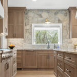 Light stained kitchen cabinets on stone wall.
