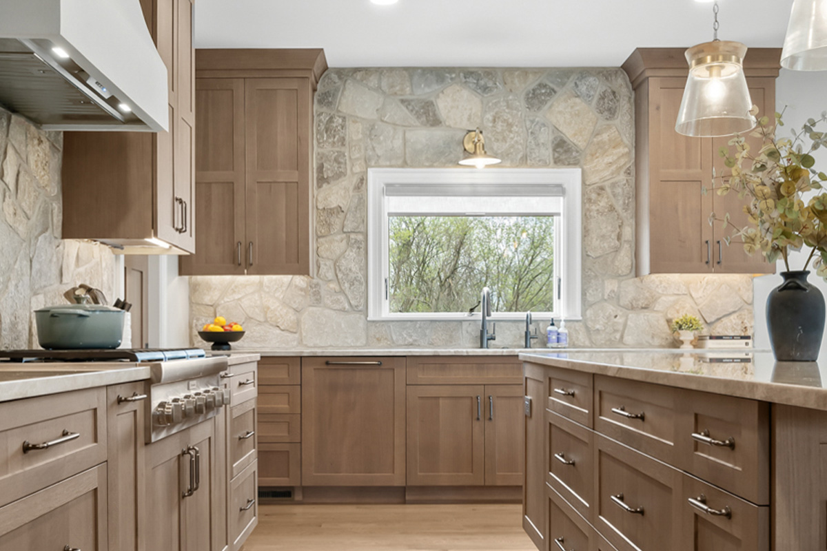Light stained kitchen cabinets on stone wall.