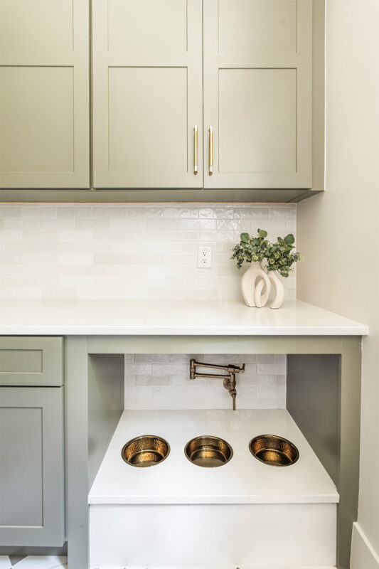 Light green mudroom cabinets with dog dish area under the counter.