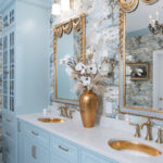 Light blue bathroom vanity cabinets with ornate gold mirrors and sink hardware.