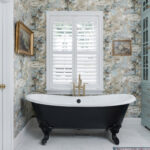 Black standalone tub with flowered wall paper.