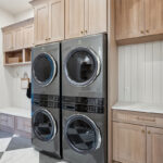 Light stained laundry cabinets with double stacked washer and dryer.