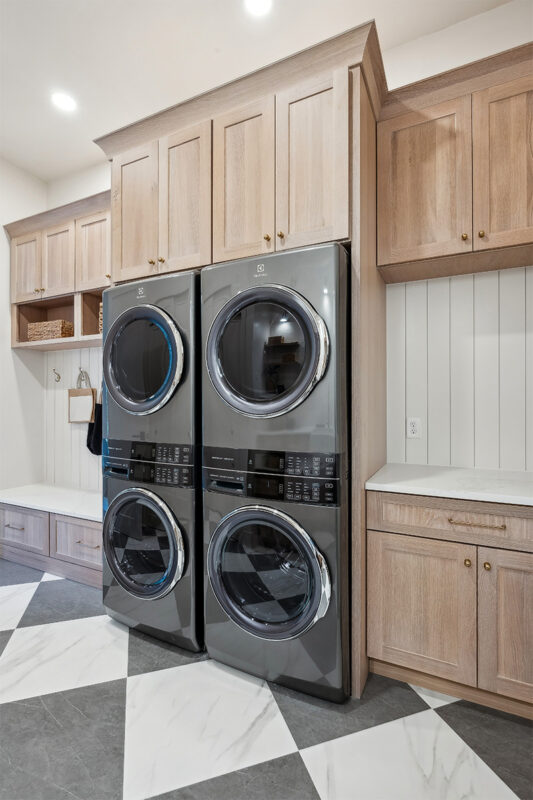 Light stained laundry cabinets with double stacked washer and dryer.