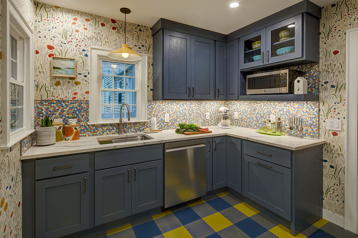 Blue kitchen cabinets with blue and yellow checkered floor and colorful backsplash.
