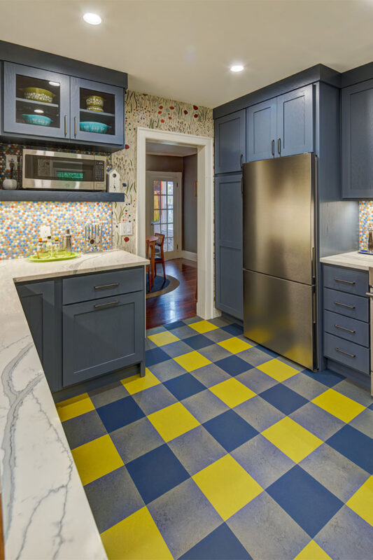 Blue kitchen cabinets with blue and yellow checkered floor and colorful backsplash.