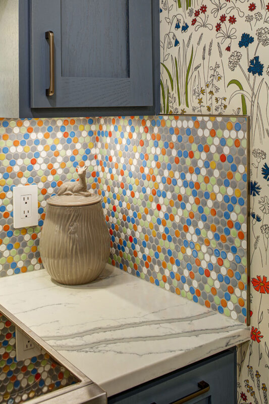 Blue kitchen cabinets with blue and yellow checkered floor and colorful backsplash.