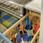 Blue kitchen cabinets with blue and yellow checkered floor and colorful backsplash.