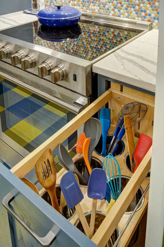 Blue kitchen cabinets with blue and yellow checkered floor and colorful backsplash.