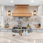 White kitchen with marble counter tops and backsplash with stained wood hood.