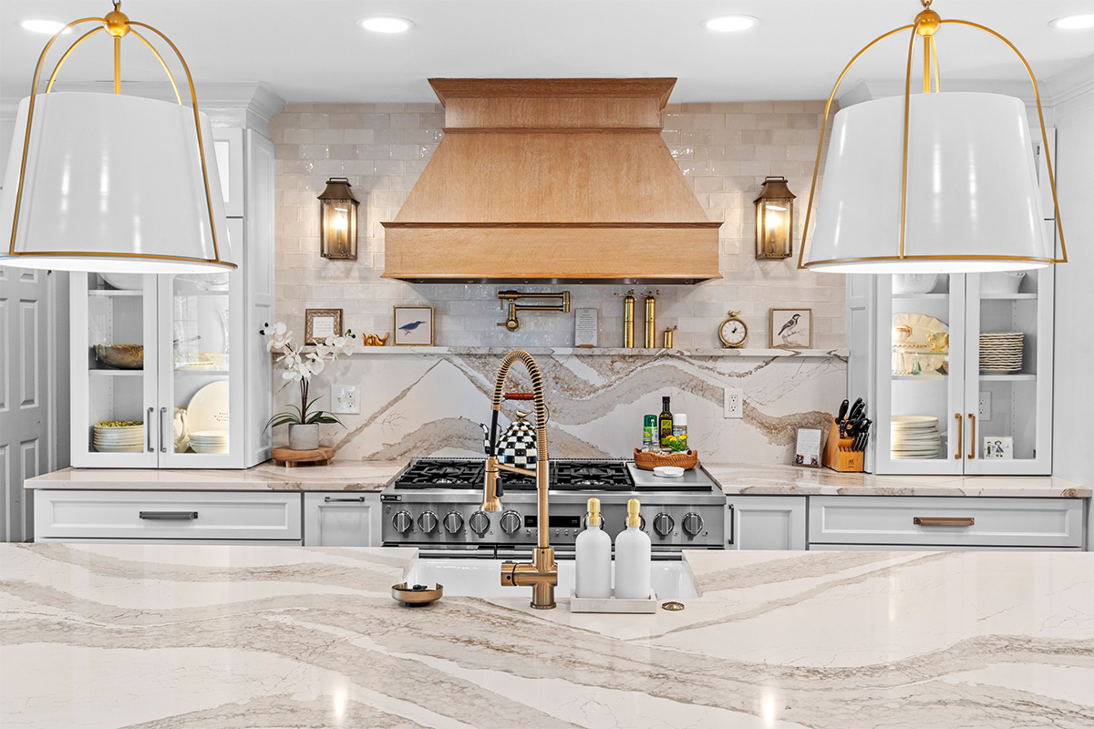 White kitchen with marble counter tops and backsplash with stained wood hood.